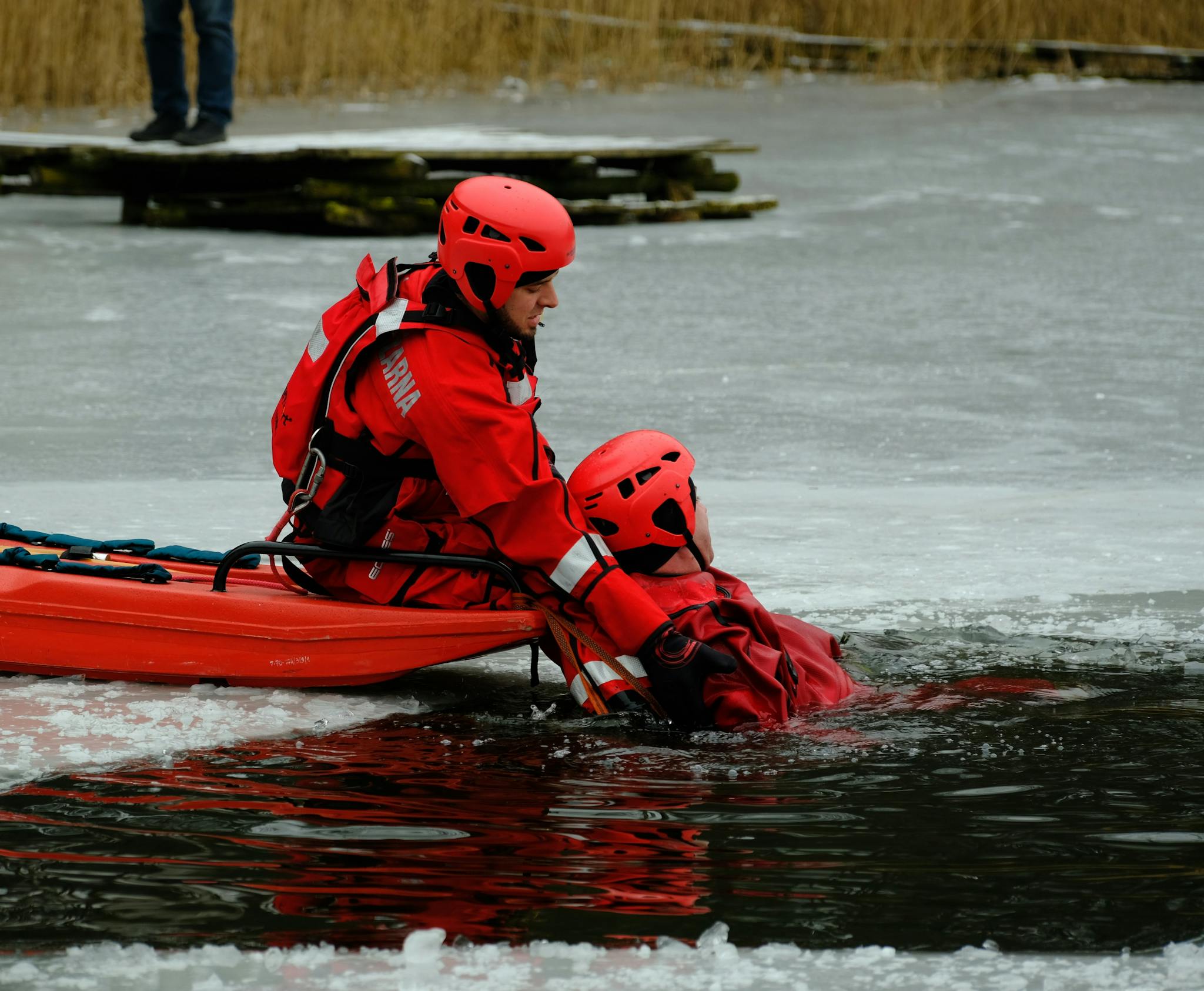 Emergency responders in action performing ice rescue training on a frozen lake wearing red safety gear.