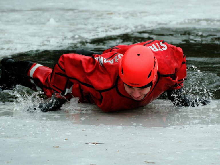 Rescue worker in red gear practicing ice rescue techniques on a frozen lake.