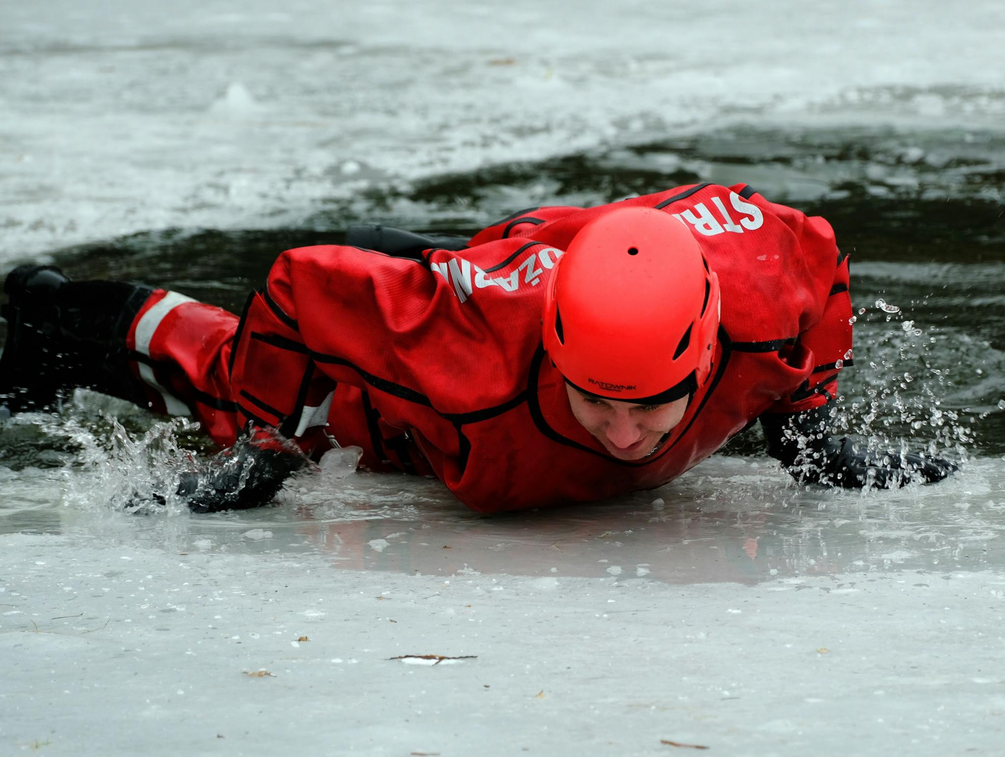 Rescue worker in red gear practicing ice rescue techniques on a frozen lake.